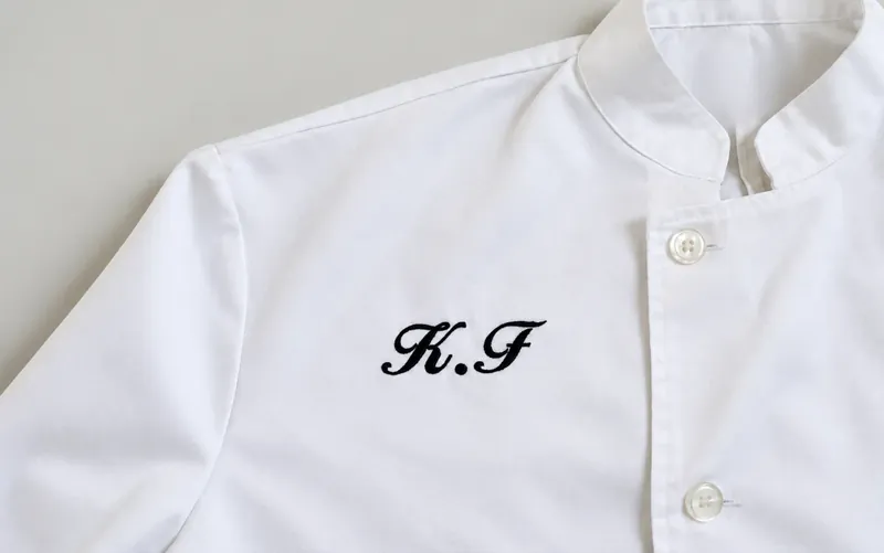 White shirt with script initials embroidered on the chest